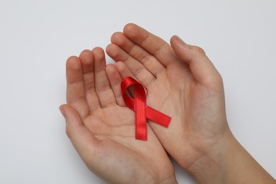Photo of Little girl holding red ribbon on white background, closeup. AIDS disease awareness