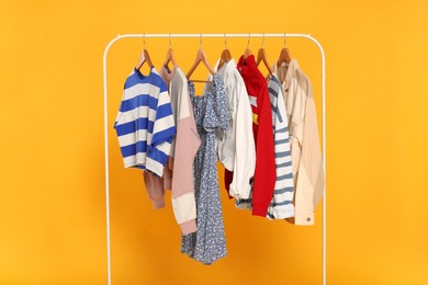 Photo of Rack with stylish women's clothes on wooden hangers against orange background