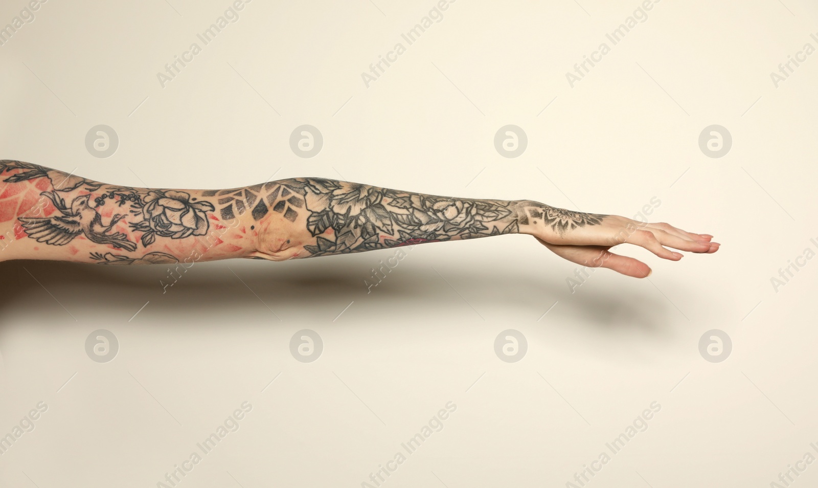 Photo of Woman with colorful tattoos on arm against white background, closeup