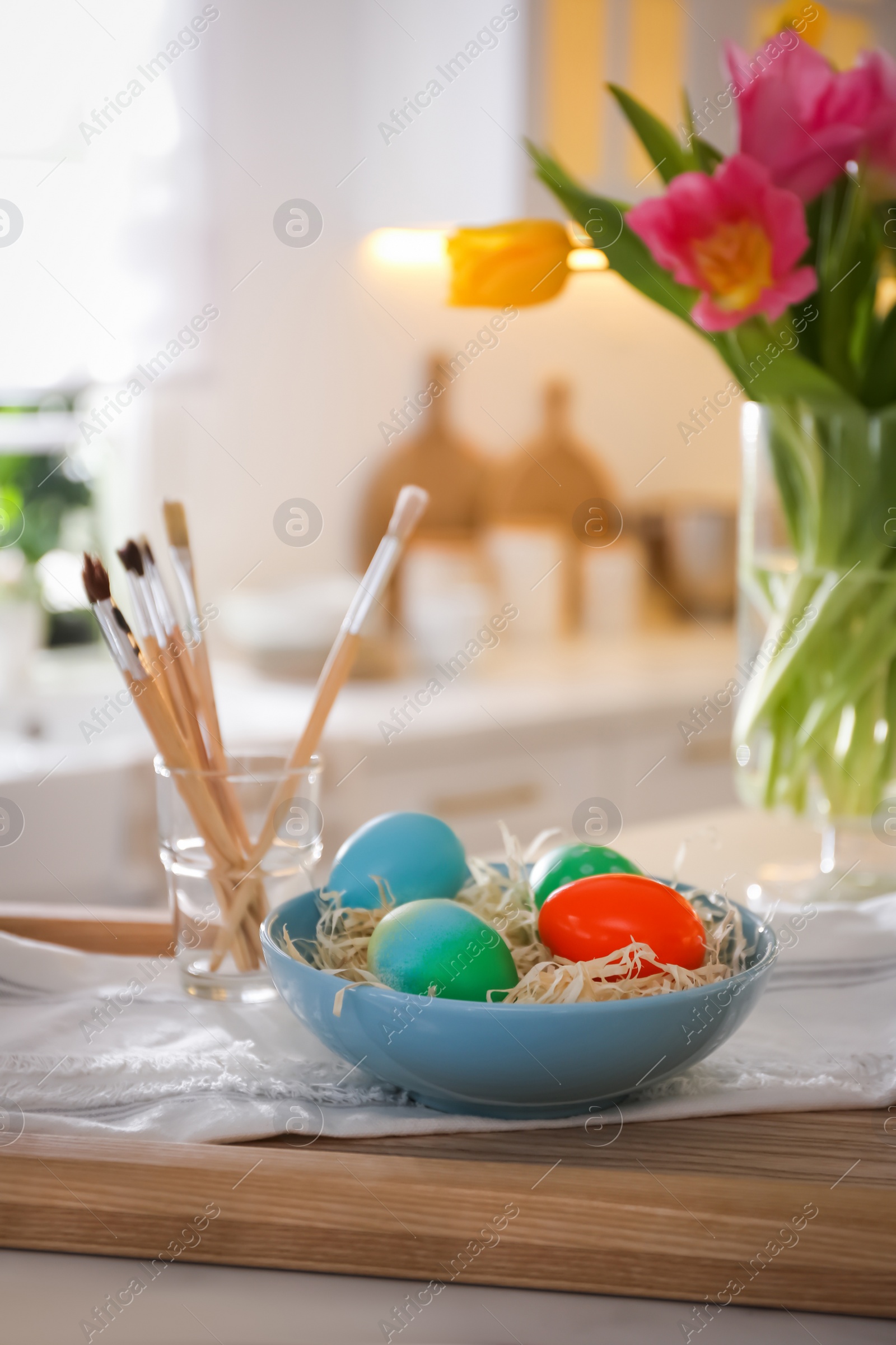 Photo of Beautifully painted Easter eggs in bowl and brushes on table indoors