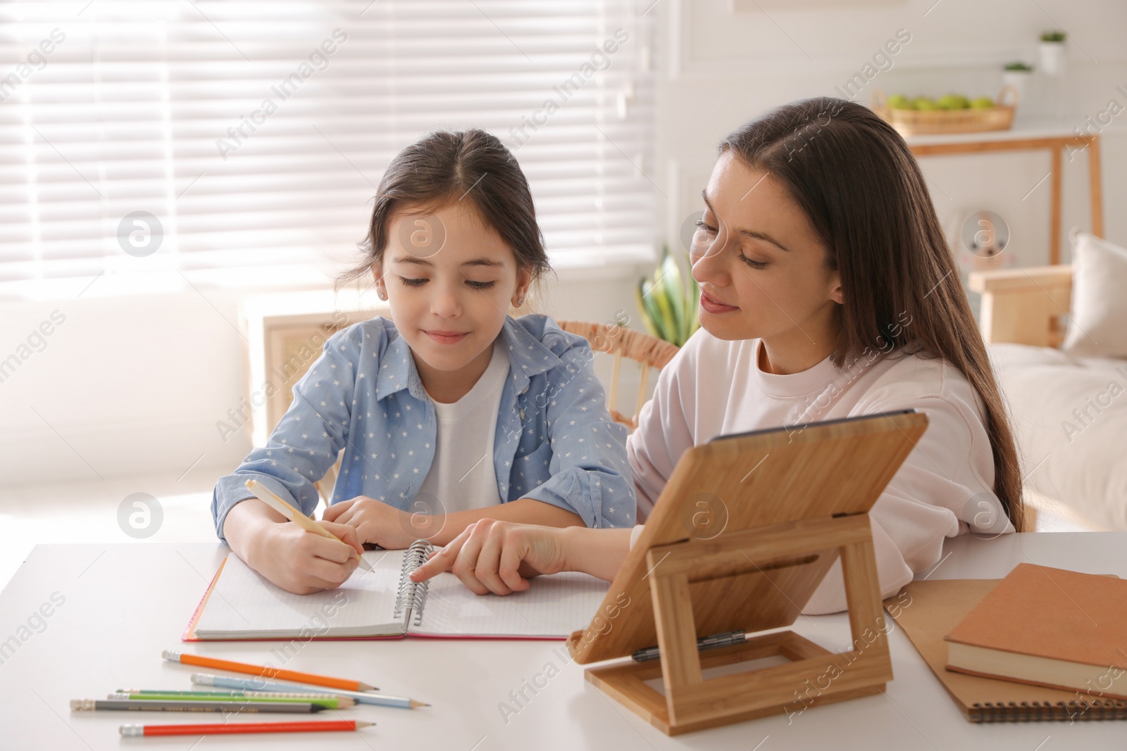 Photo of Mother helping her daughter with homework using tablet at home