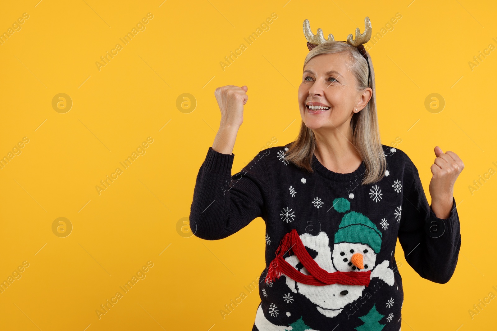 Photo of Happy senior woman in Christmas sweater and deer headband on orange background. Space for text