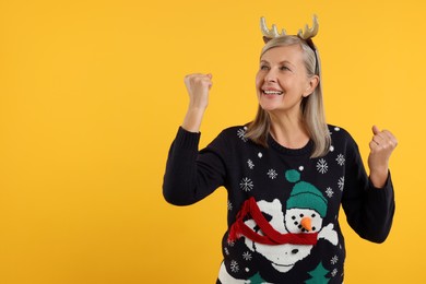 Happy senior woman in Christmas sweater and deer headband on orange background. Space for text