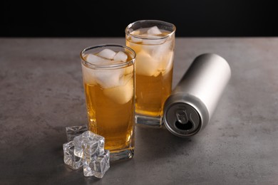 Photo of Energy drink in glasses, aluminium can and ice cubes on grey table