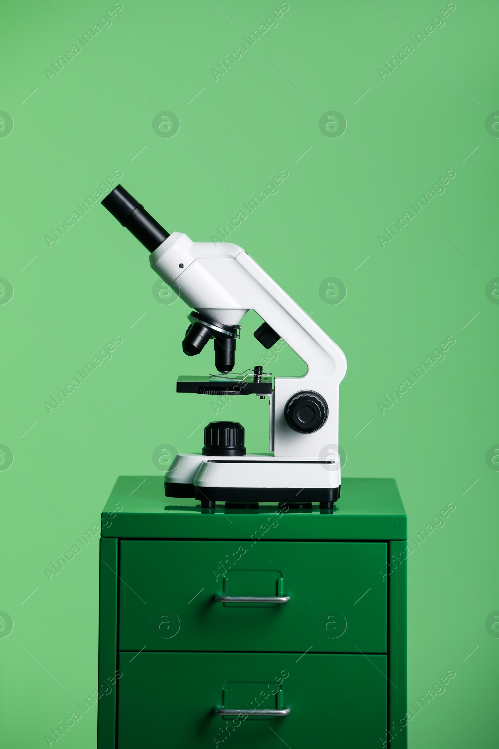 Photo of Modern medical microscope on lab drawer against green background