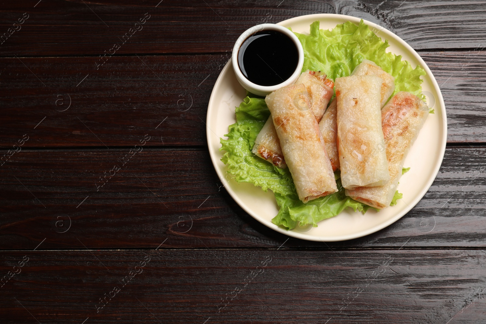 Photo of Delicious fried spring rolls with soy sauce on wooden table, top view. Space for text