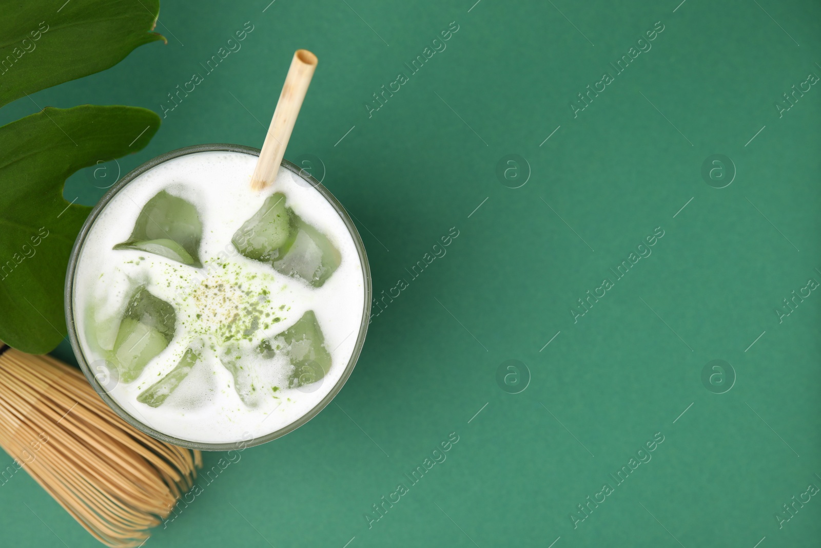 Photo of Glass of tasty iced matcha latte, leaf and bamboo whisk on green background, flat lay. Space for text