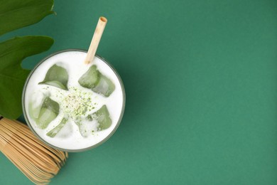 Photo of Glass of tasty iced matcha latte, leaf and bamboo whisk on green background, flat lay. Space for text