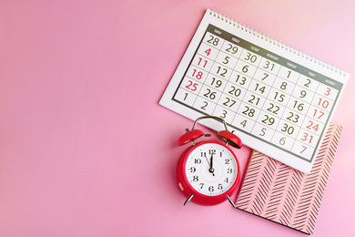 Calendar, notebook and alarm clock on pink background, flat lay. Space for text