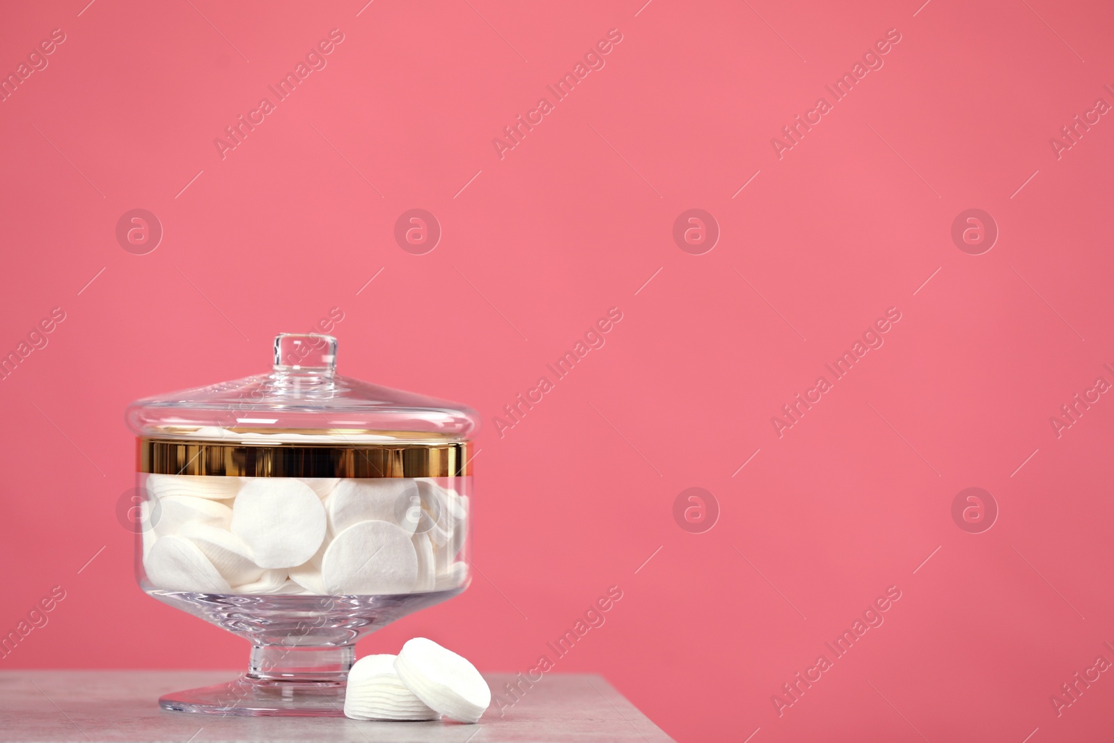 Photo of Glass jar with cotton pads on table against pink background. Space for text