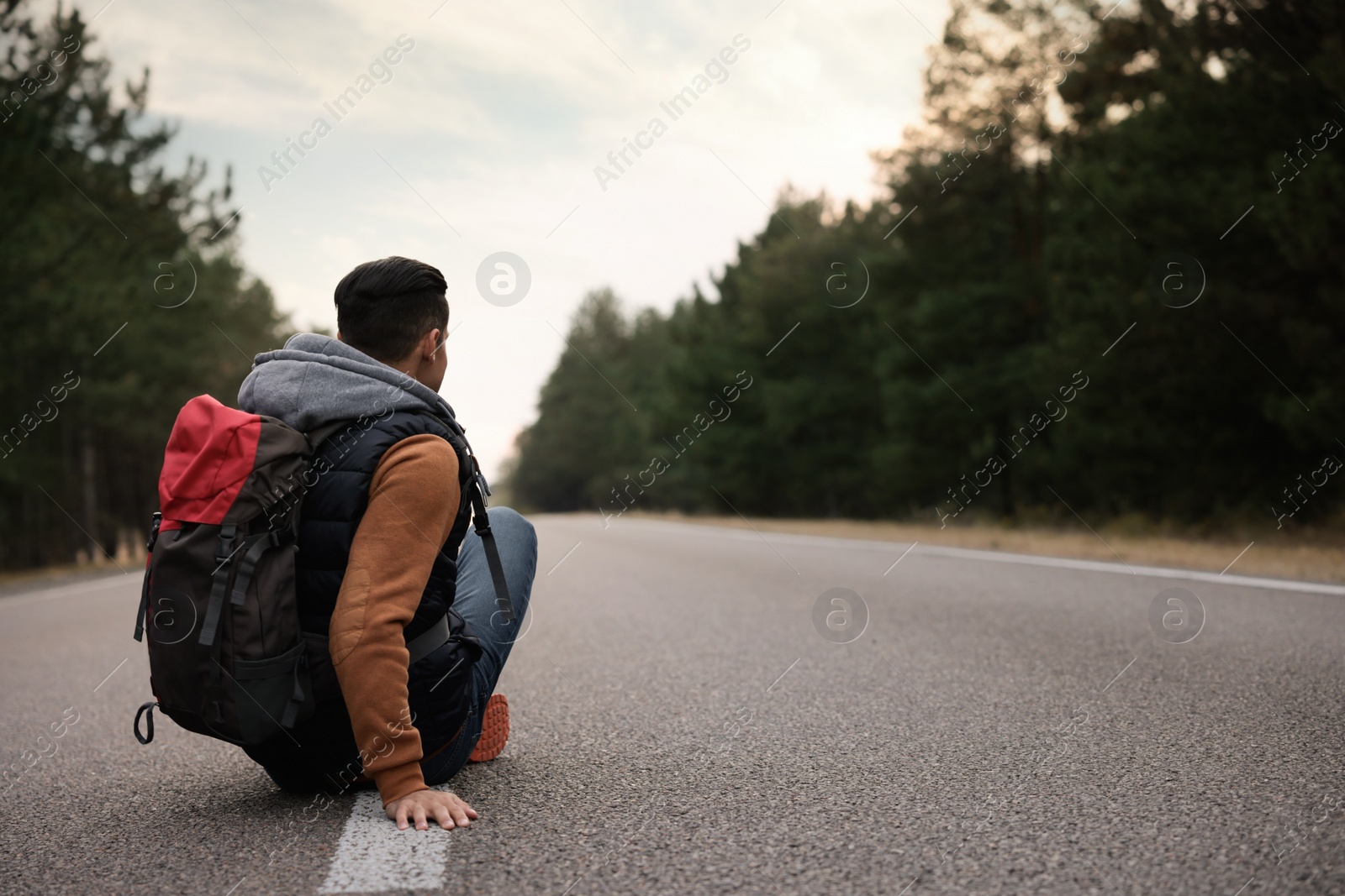 Photo of Man with backpack sitting on road near forest, back view