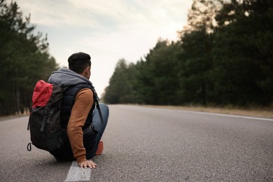 Man with backpack sitting on road near forest, back view