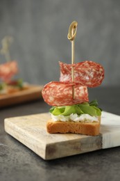 Photo of Tasty canape with salami, greens and cream cheese on grey table