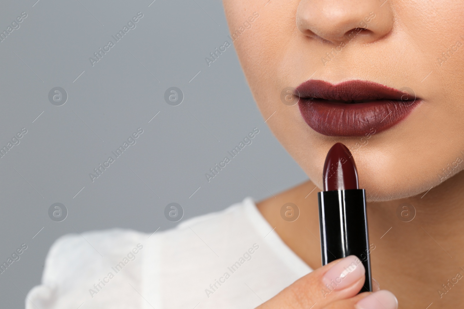 Photo of Young woman applying beautiful lipstick on gray background, closeup. Space for text