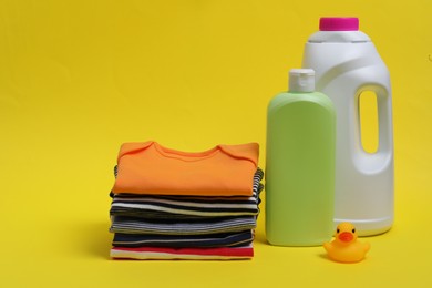 Photo of Laundry detergents, stack of baby clothes and rubber duck on yellow background. Space for text