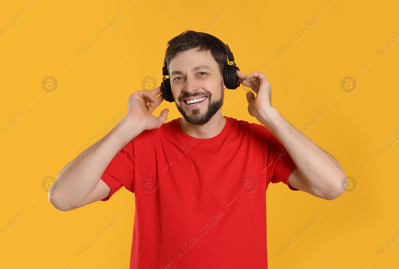 Photo of Happy man in headphones enjoying music on orange background
