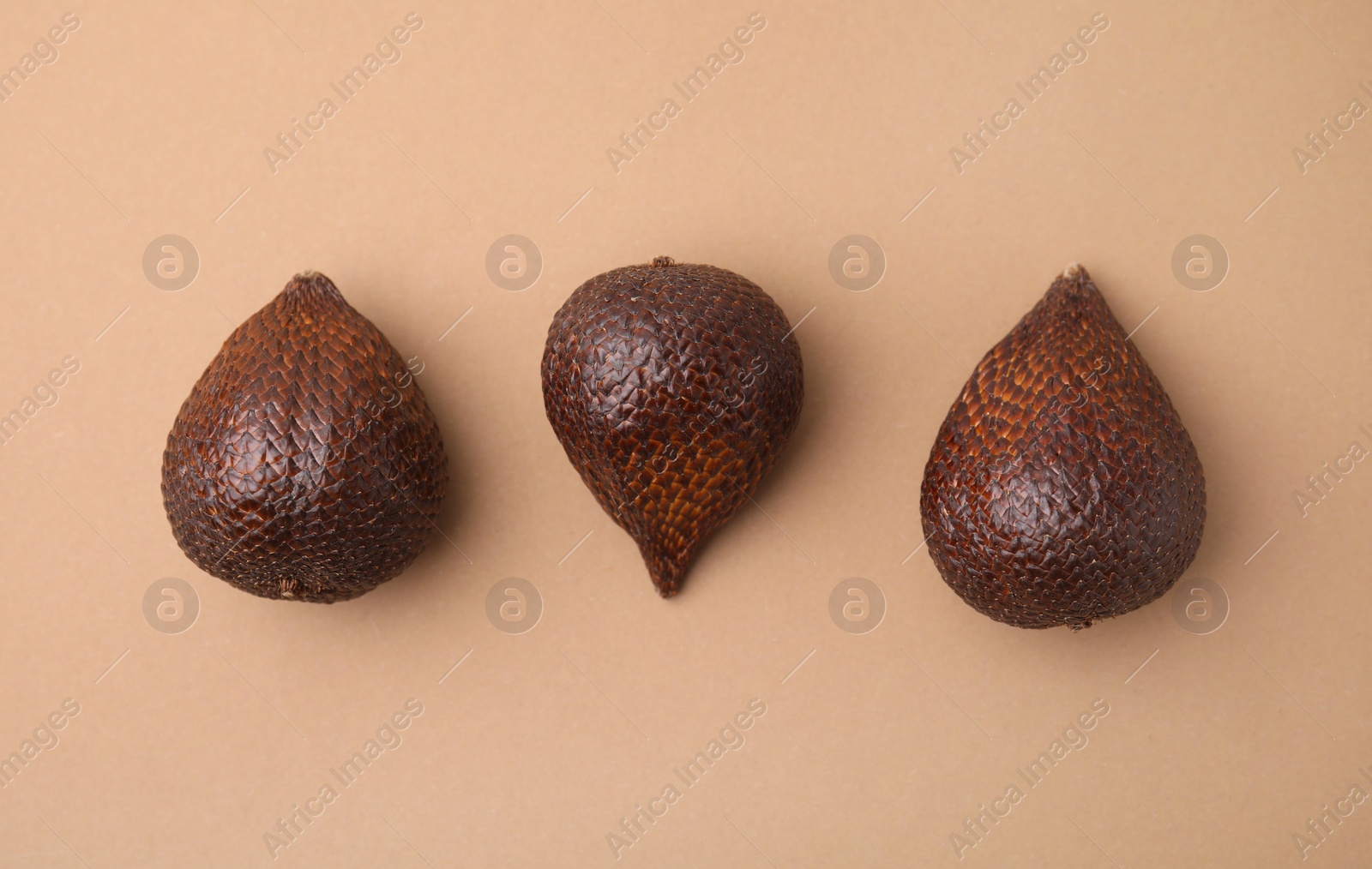 Photo of Three salak fruits on pale brown background, flat lay