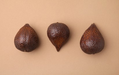 Three salak fruits on pale brown background, flat lay