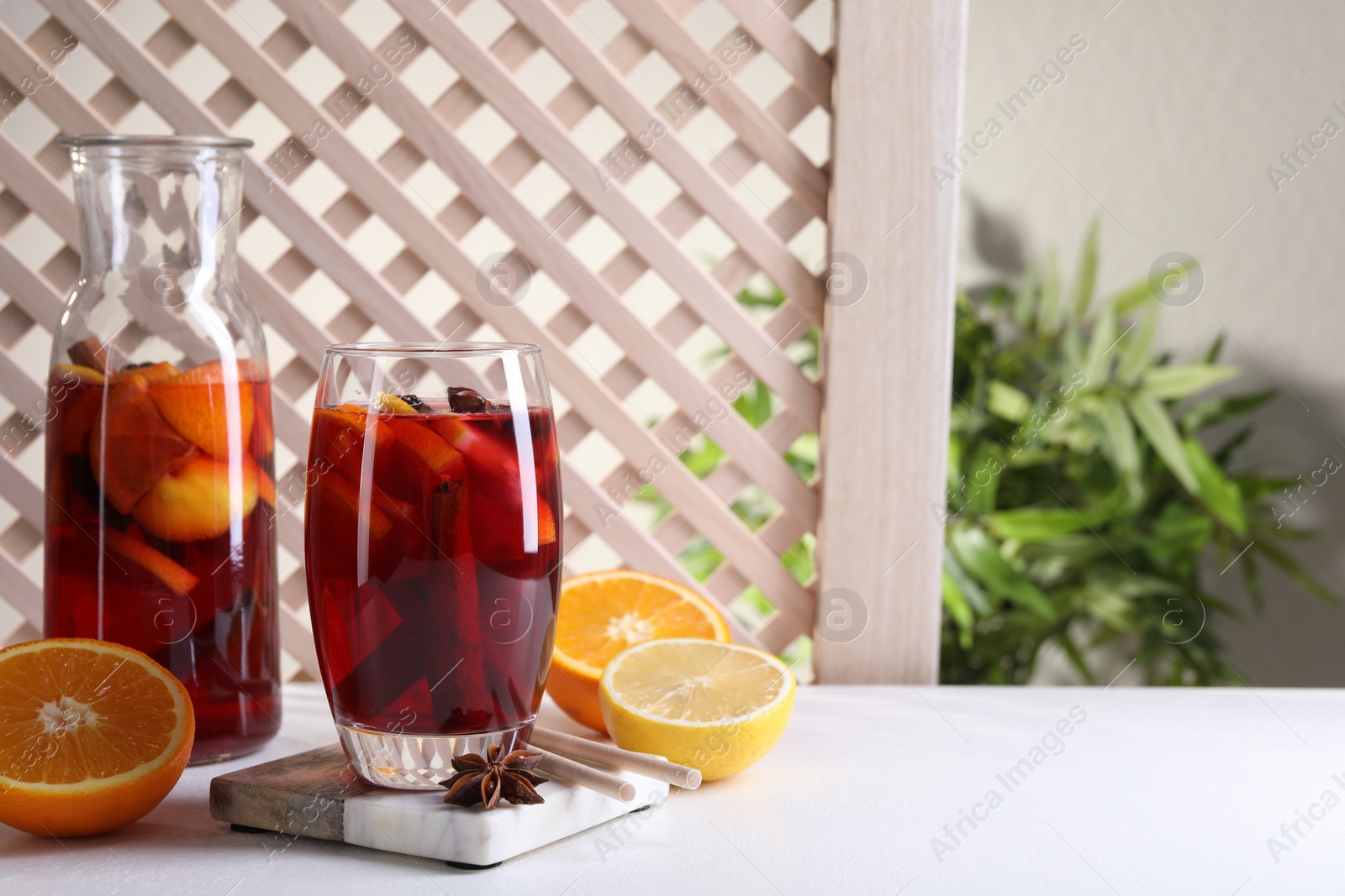 Photo of Aromatic punch drink and ingredients on white table. Space for text