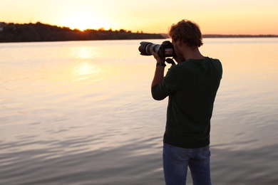 Male photographer taking photo of riverside sunset with professional camera outdoors