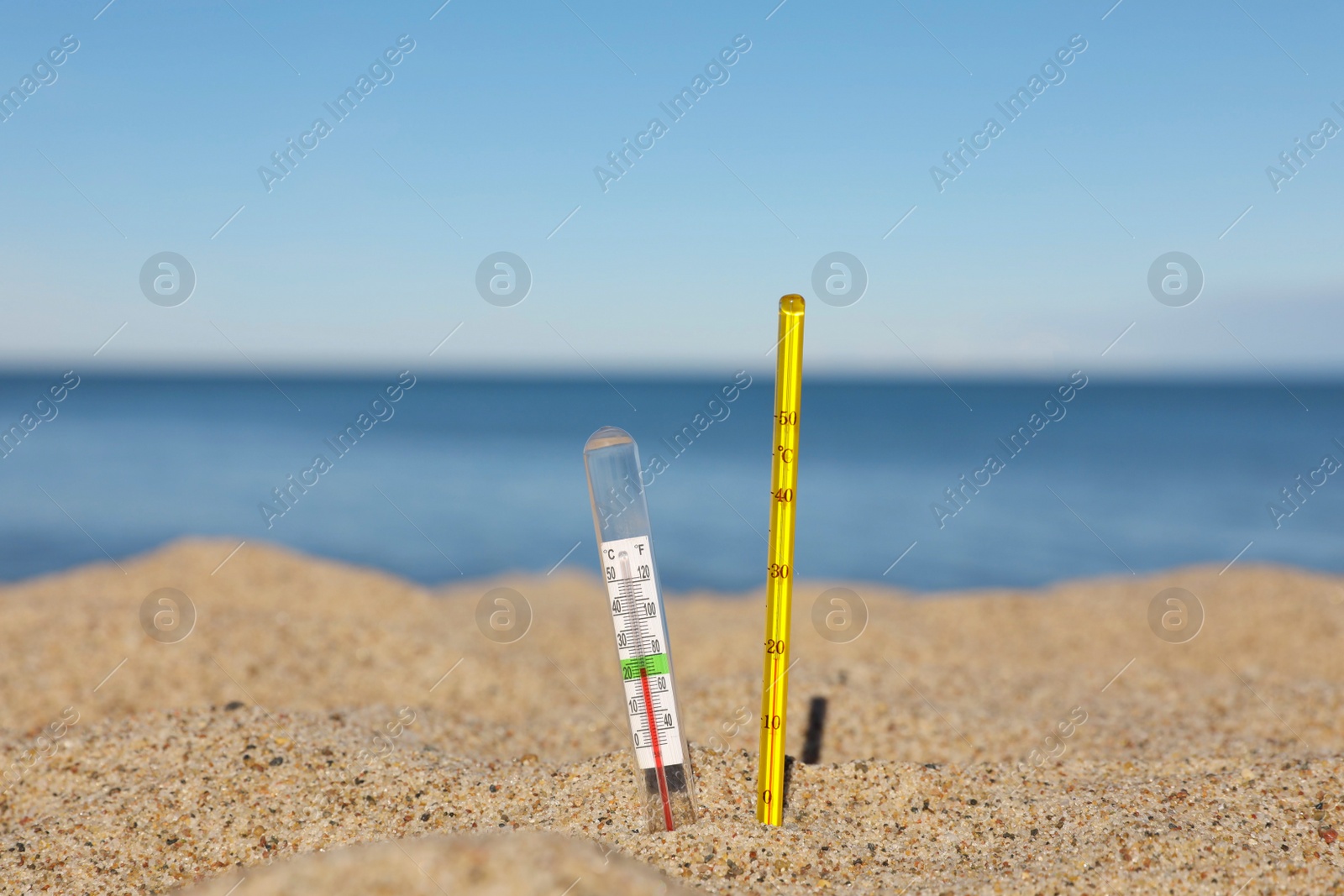 Photo of Different weather thermometers in sand near sea