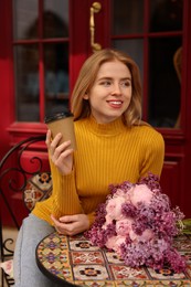 Beautiful woman with bouquet of spring flowers and coffee in outdoor cafe