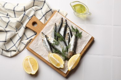 Photo of Fresh raw sprats, dill, oil and cut lemon on white tiled table, flat lay