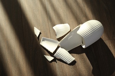 Photo of Broken white ceramic vase on wooden floor, above view
