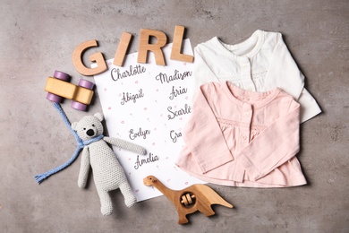 Photo of List of baby names, toys and child's clothes on grey table, flat lay