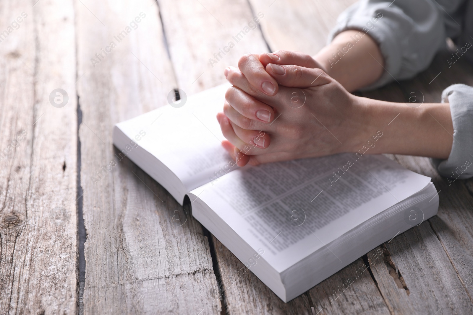 Photo of Religion. Christian woman praying over Bible at wooden table, closeup