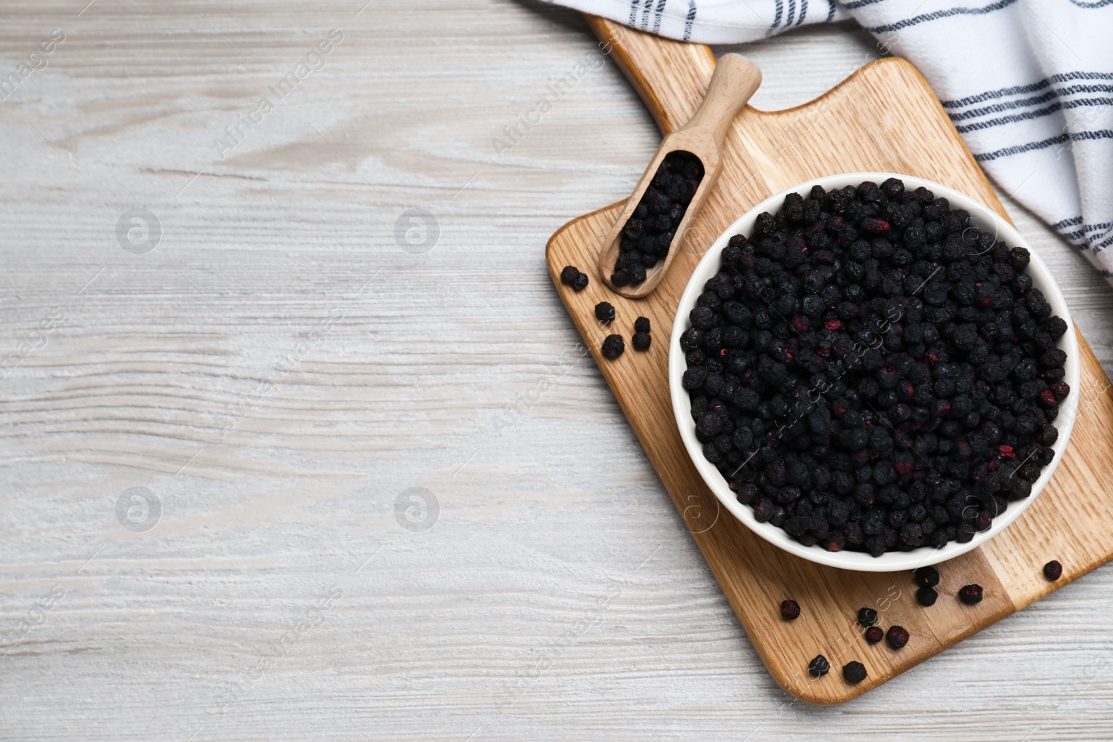 Photo of Bowl and scoop with dried blueberries on white wooden table, top view. Space for text