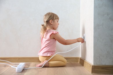 Photo of Little child playing with electrical socket and power strip plug at home. Dangerous situation