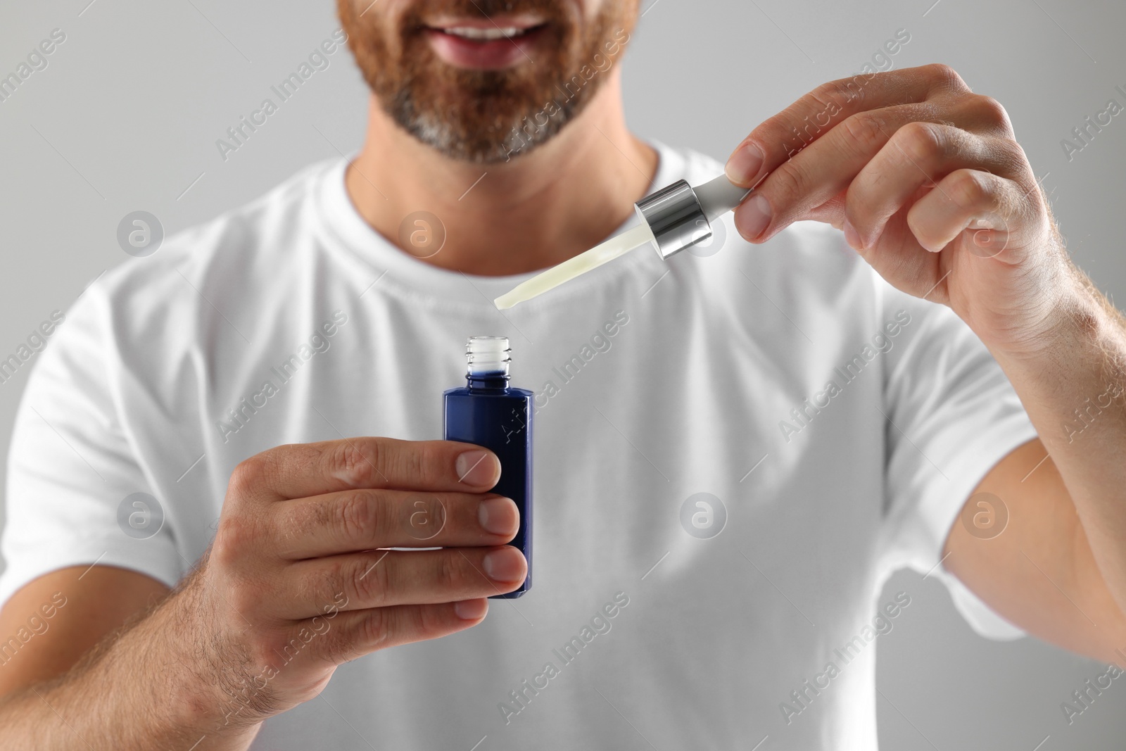 Photo of Man with cosmetic serum on light grey background, closeup