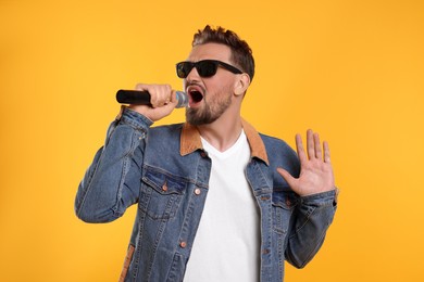 Photo of Handsome man with sunglasses and microphone singing on yellow background