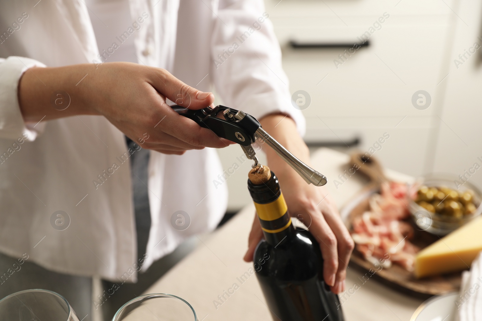 Photo of Woman opening wine bottle with corkscrew at table indoors, closeup