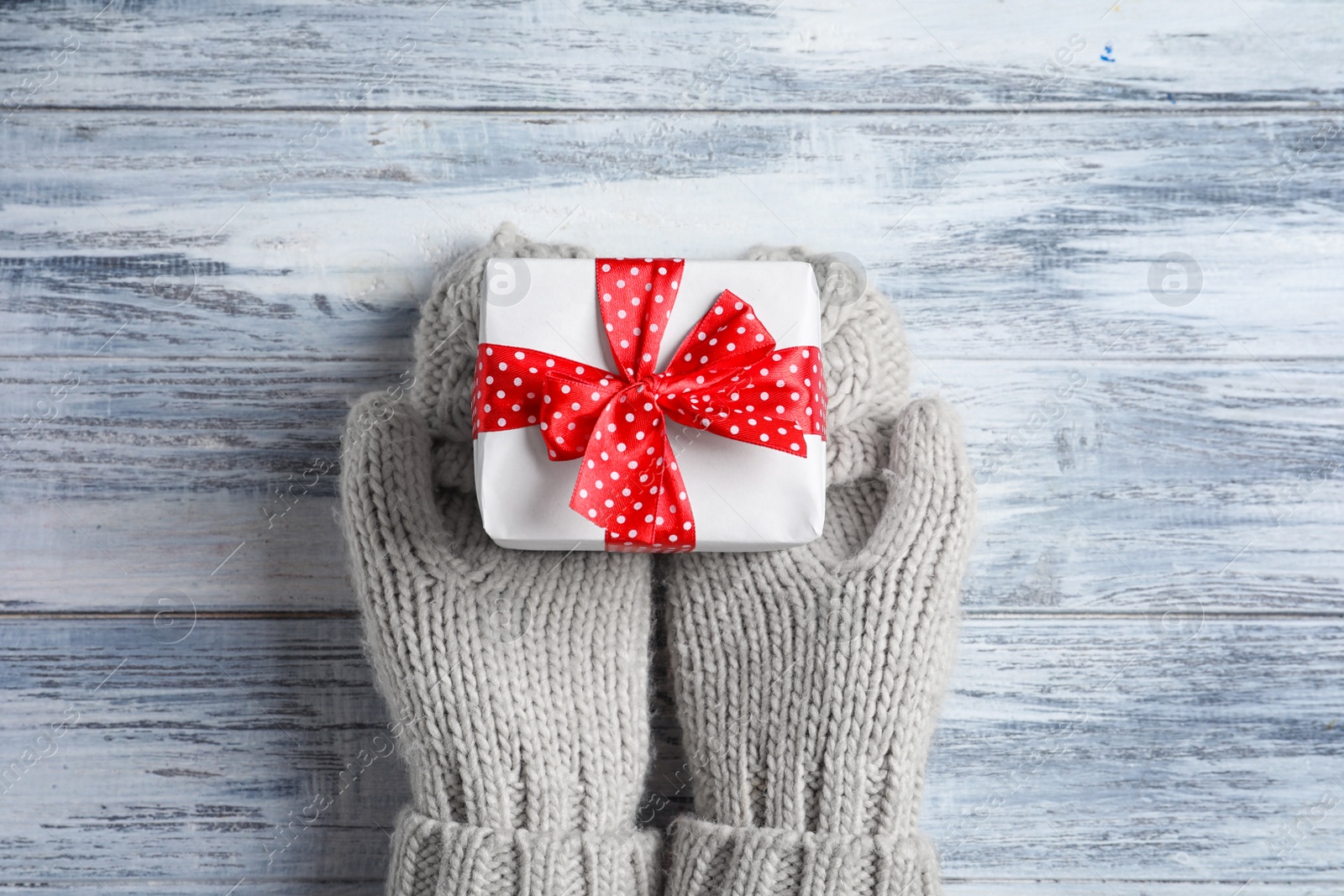 Photo of Woman wearing warm mittens holding Christmas gift on wooden background, top view