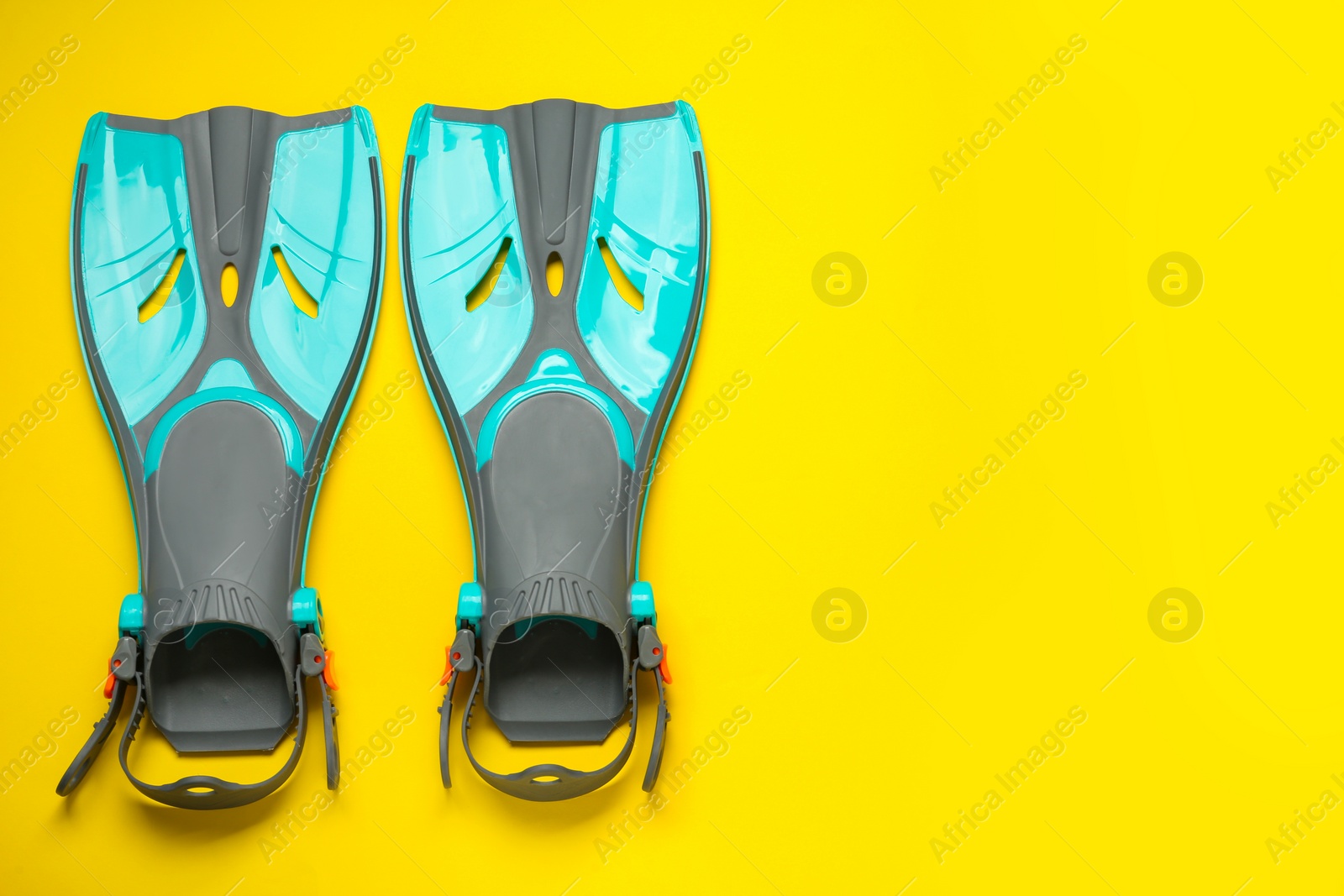 Photo of Pair of turquoise flippers on yellow background, flat lay. Space for text