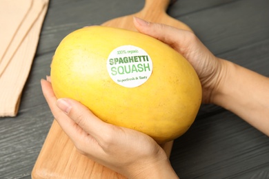 Woman holding ripe spaghetti squash on wooden table, closeup