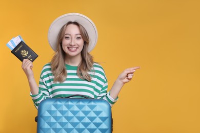 Photo of Happy young woman with passport, ticket and suitcase pointing at something on yellow background, space for text