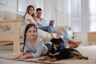 Photo of Little girl with puppy lying while parents sitting on sofa in living room