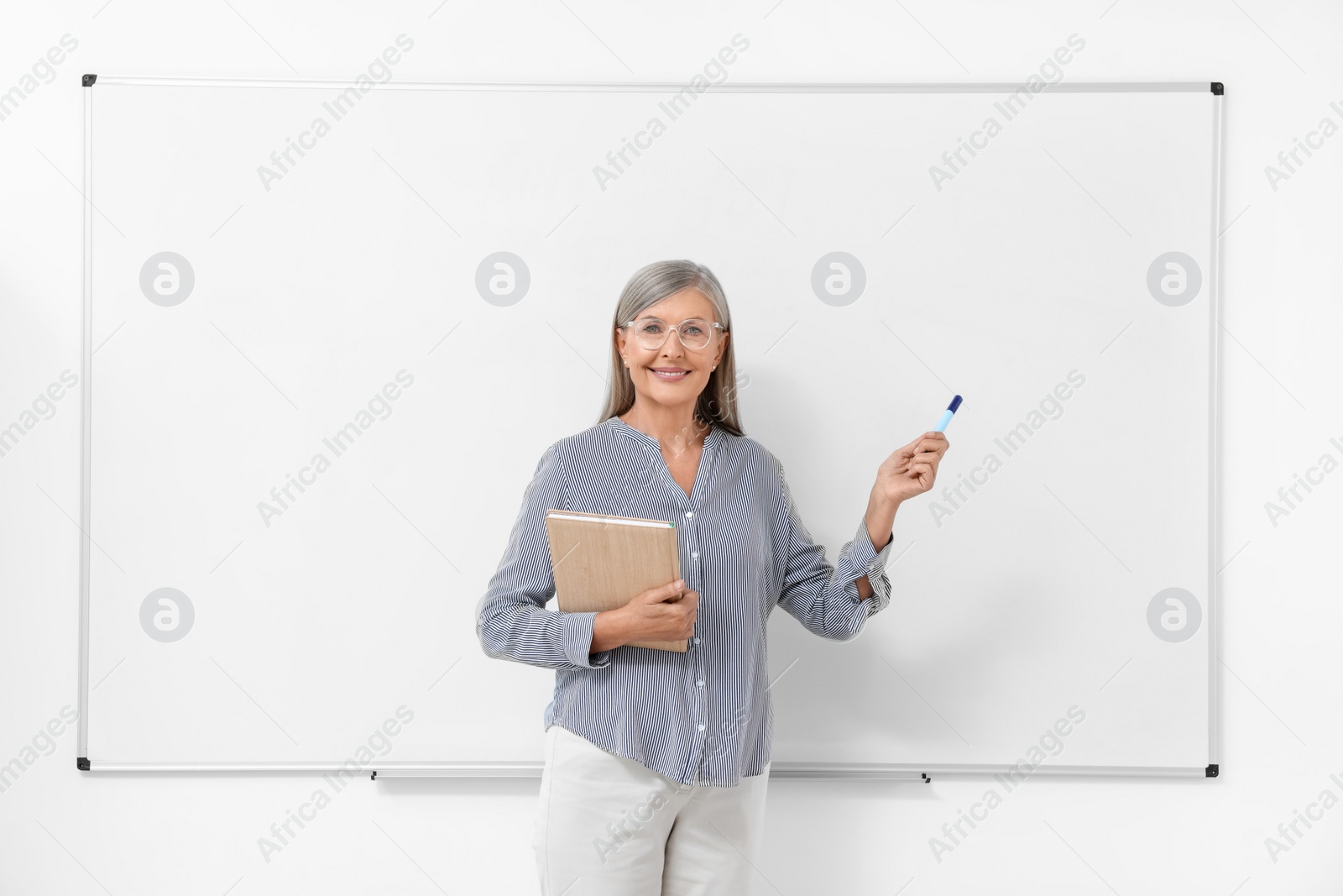 Photo of Professor with notebook and marker giving lecture near whiteboard indoors