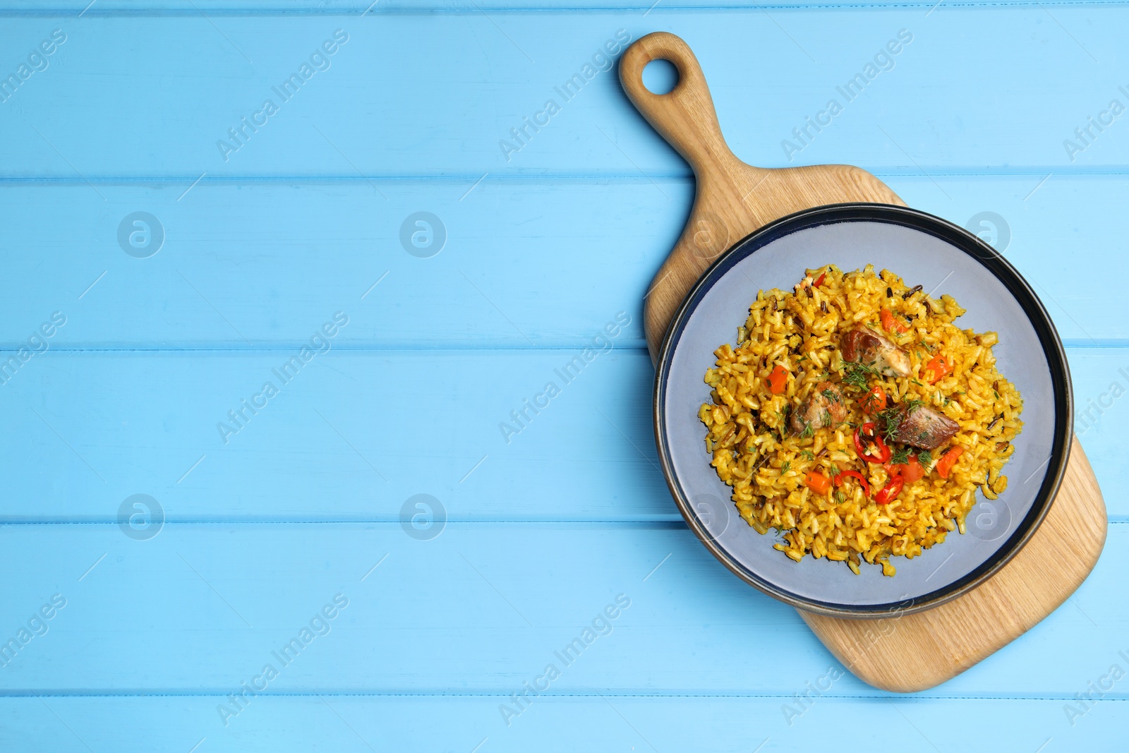 Photo of Delicious pilaf with meat, carrot and chili pepper on light blue wooden table, top view. Space for text