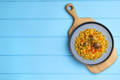 Photo of Delicious pilaf with meat, carrot and chili pepper on light blue wooden table, top view. Space for text