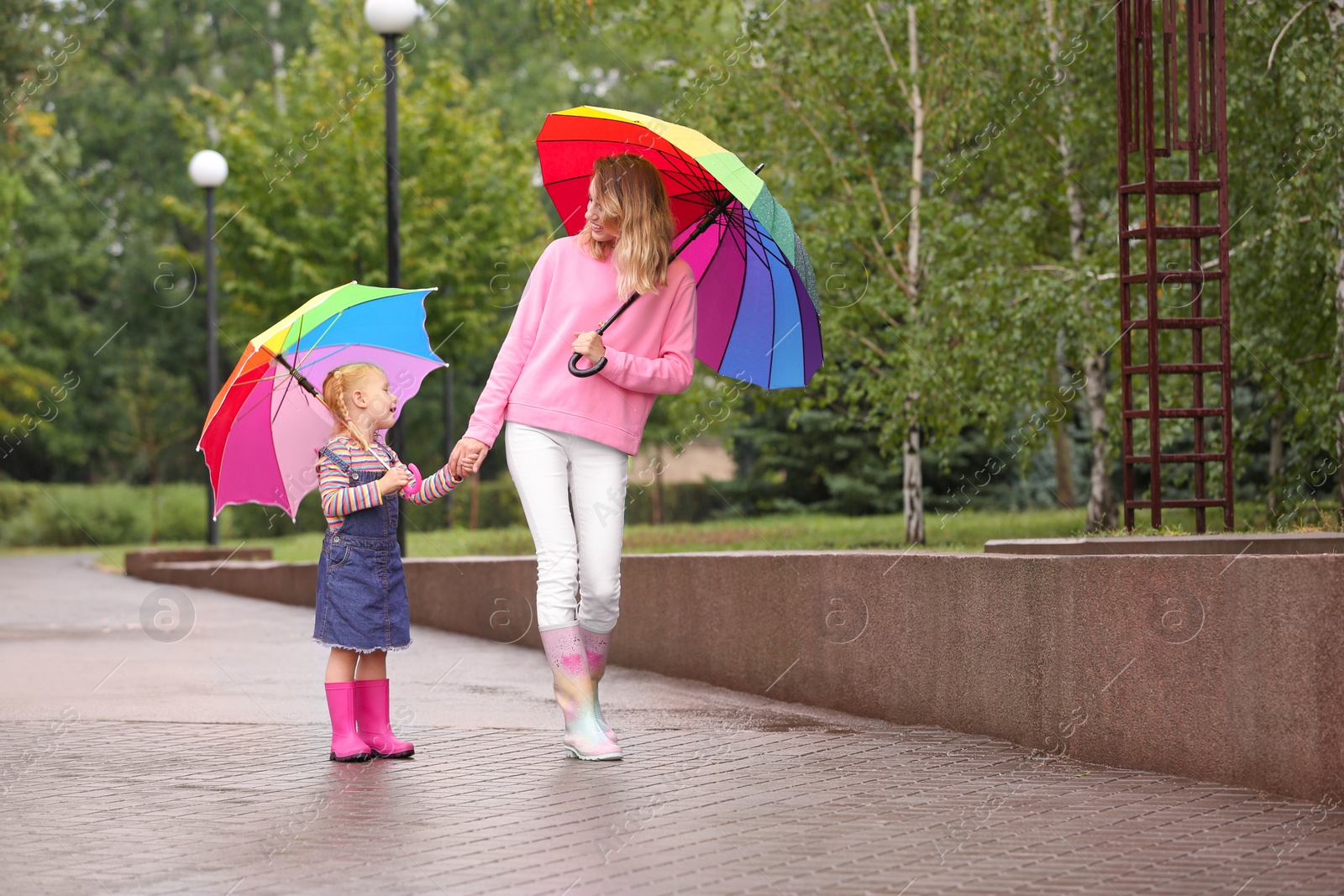 Photo of Happy mother and daughter with bright umbrellas walking in park