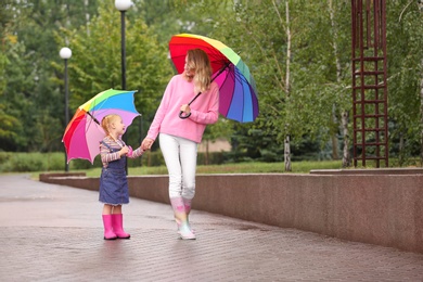 Happy mother and daughter with bright umbrellas walking in park