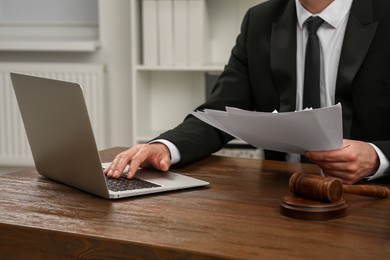 Law and justice. Lawyer working with documents and laptop at wooden table in office, closeup