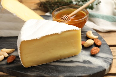 Photo of Tasty Camembert cheese with honey and nuts on wooden table, closeup