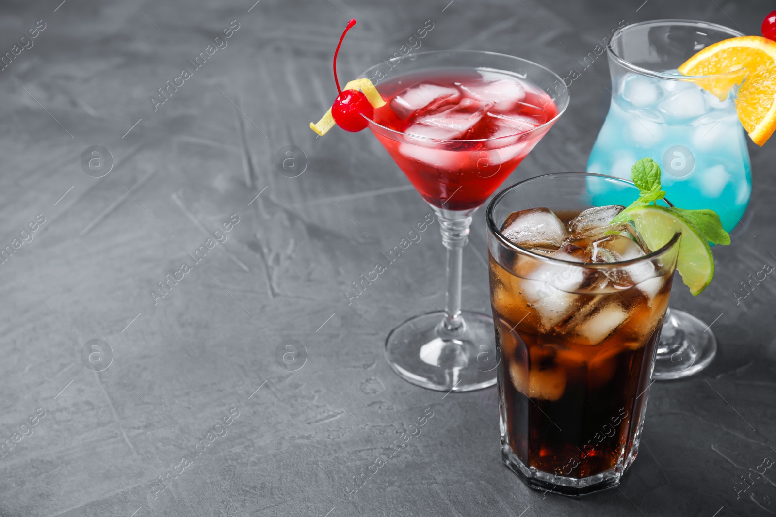 Photo of Tasty refreshing cocktails in glasses on grey stone table, space for text