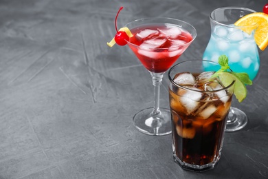 Photo of Tasty refreshing cocktails in glasses on grey stone table, space for text