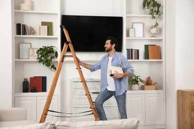 Man with books near wooden folding ladder at home